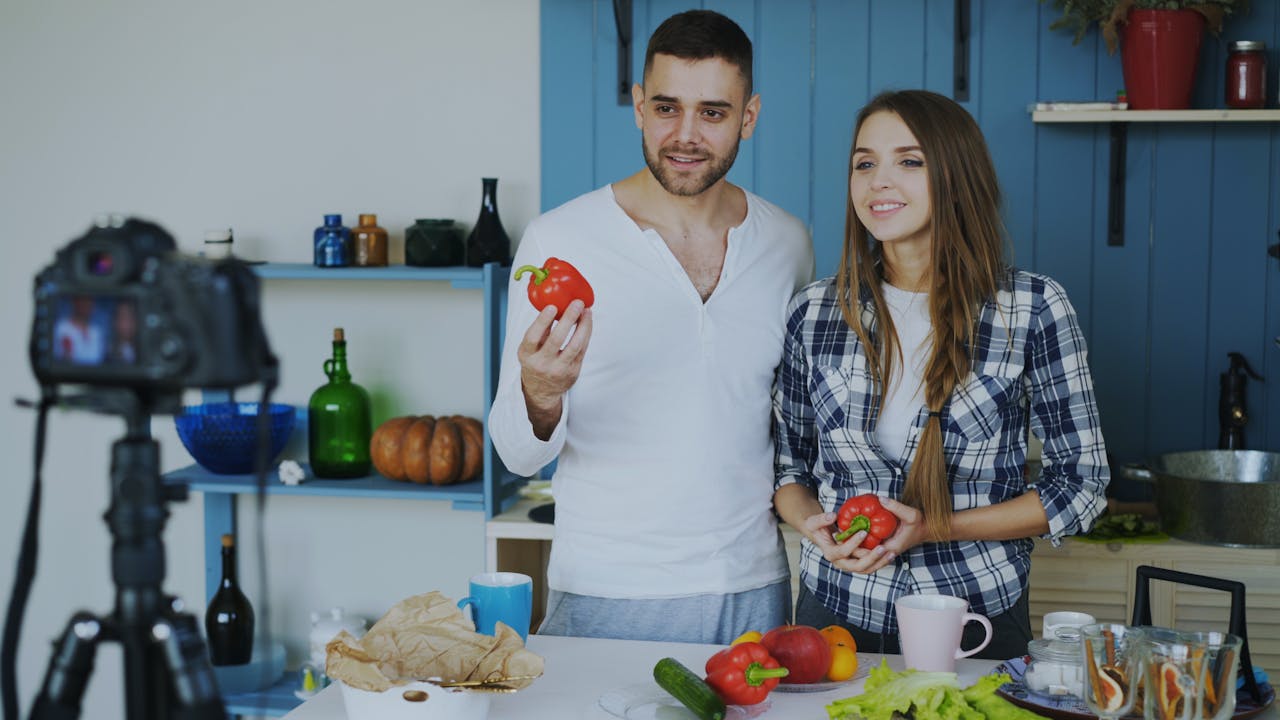 services-03 A couple prepares to film a cooking video while holding bell peppers in a stylish kitchen.