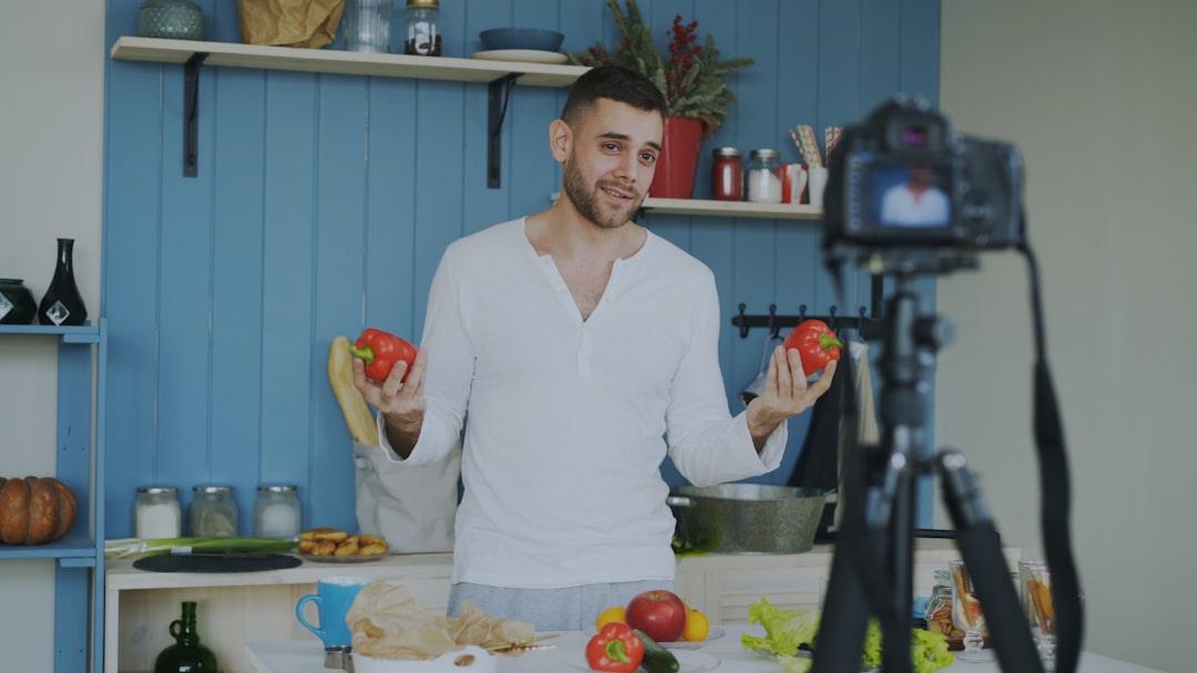Attractive cheerful man recording video blog about vegetarian healthy food on dslr camera in kitchen at home