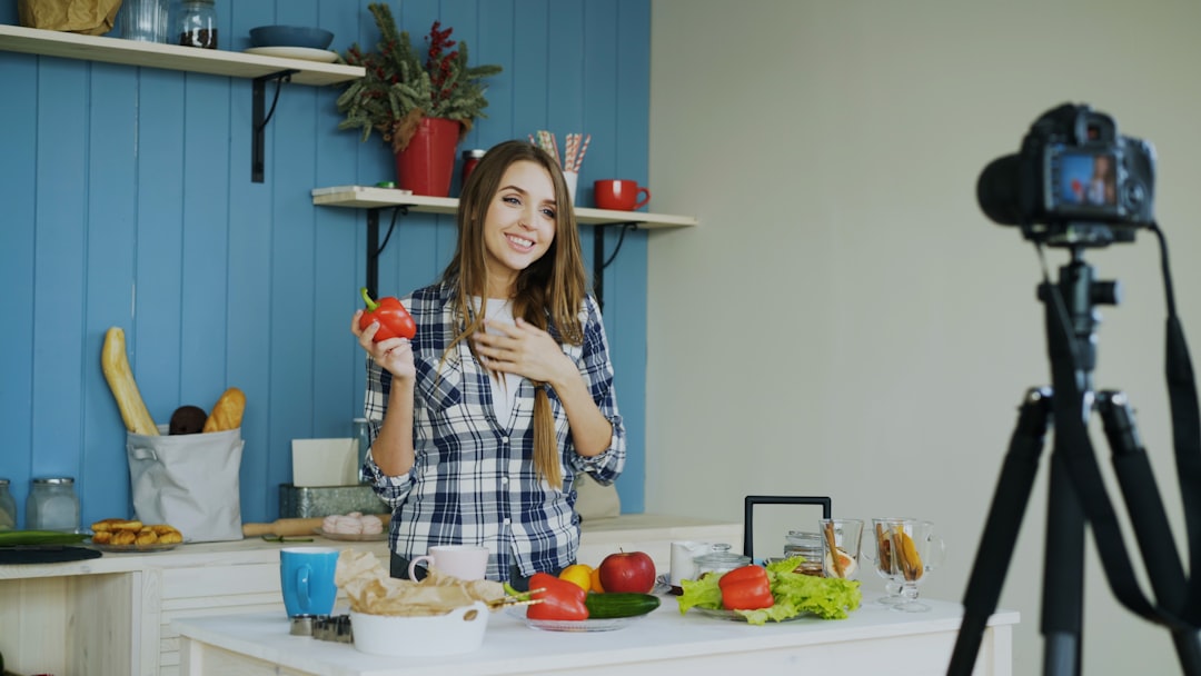 gallery-6 Young attractive woman recording video blog about vegetarian healthy food on dslr camera in kitchen at home