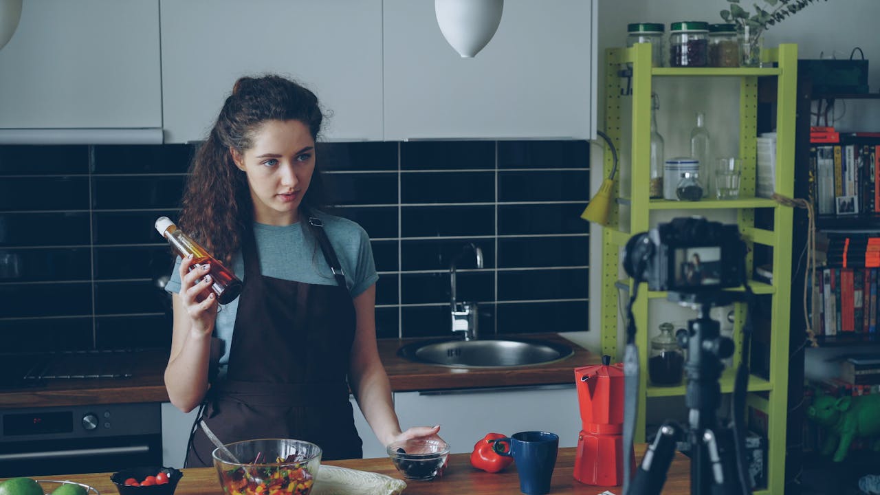 services-02 A woman filming a cooking vlog in her kitchen holding a condiment bottle.